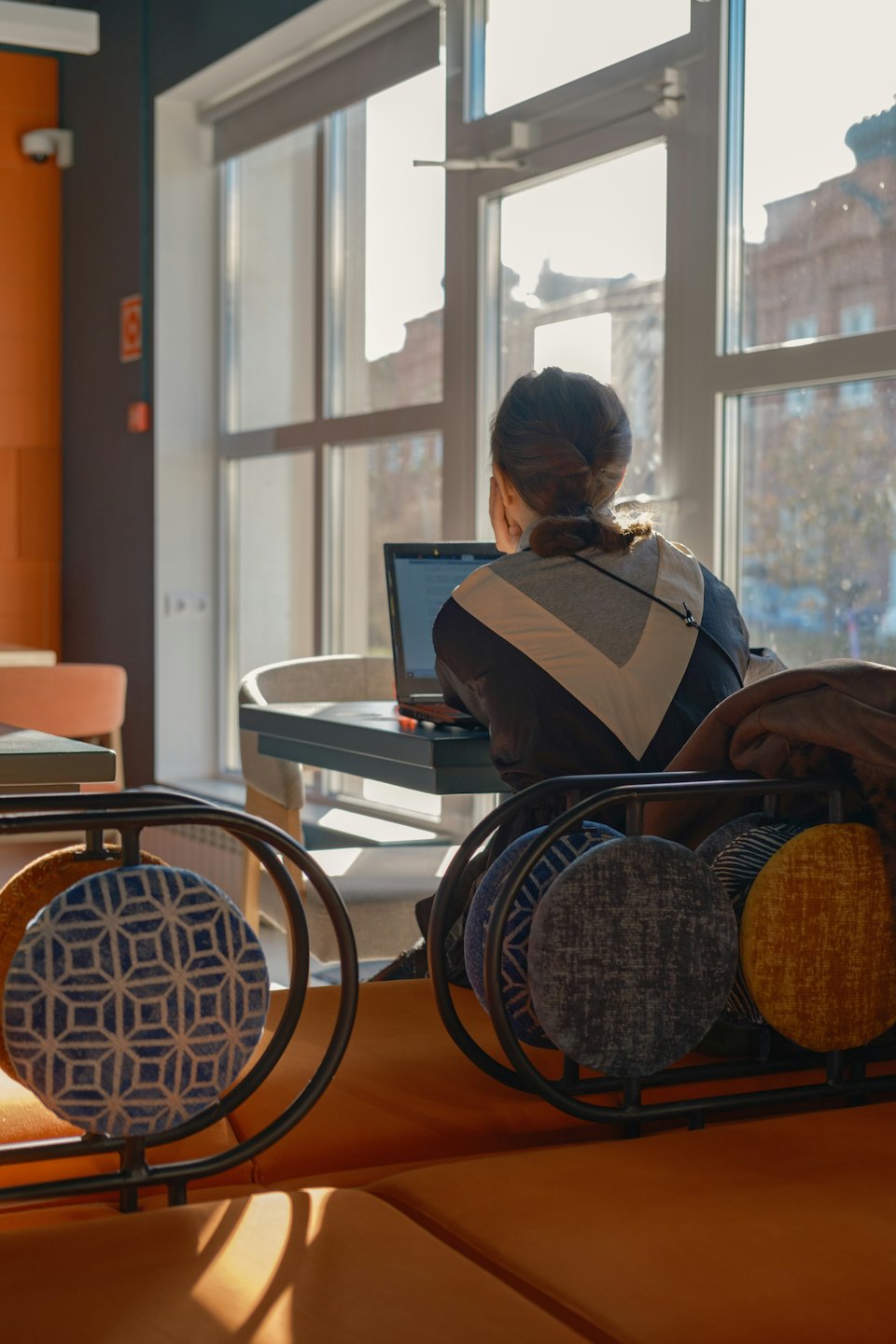 Person working on laptop at desk by large sunlit window.